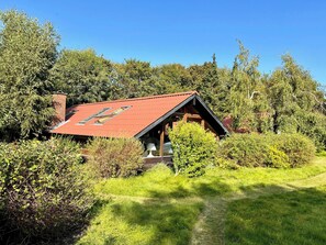 Un chalet rustique avec un toit rouge, entouré d’une végétation luxuriante et d’arbres.
