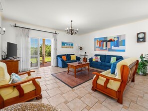 A living room with a sofa, coffee table, and chairs, a television, and a painting on the wall. - Charming Villa with Pool & Garden in Vale da Lama (Odiáxere, Lagos)