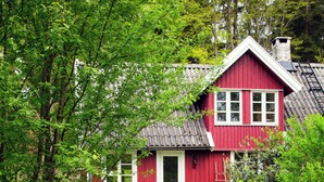 A red house with a white door, surrounded by greenery and a stone path leading to a bench. - The Hallandsåsen lighthouse, a natural retreat (Munka-ljungby)