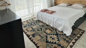 A bedroom with a bed, a wooden headboard, a window with curtains, a bedside table, and a patterned rug.
