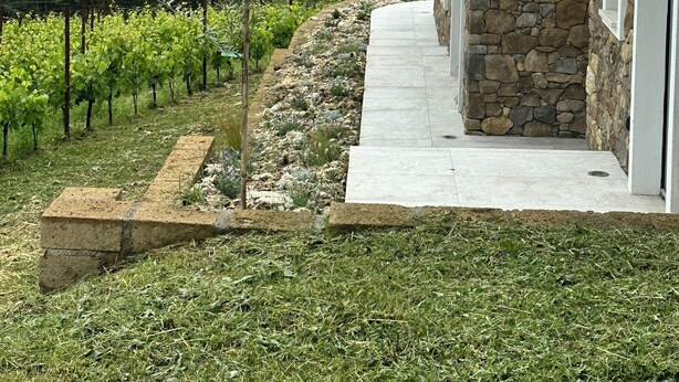 A stone building with a tiled roof, a stone wall, and a paved pathway leading to a door.