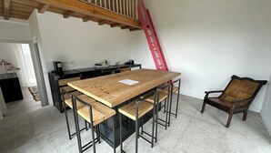 A dining area with a large wooden table, metal chairs, a red ladder, and a kitchen in the background.
