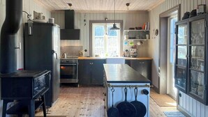 Une cuisine équipée d’une cuisinière, d’un four et de casseroles suspendues, avec un plancher en bois et une fenêtre offrant une vue agréable.