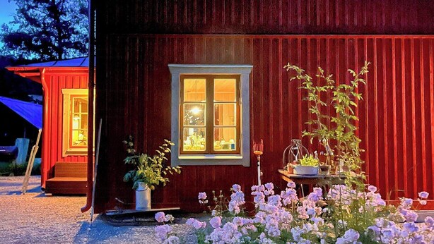 Une maison en bois rouge avec une fenêtre, une porte et un petit jardin fleuri.