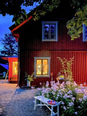Uma casa de madeira vermelha com uma janela, uma porta e um pequeno jardim com flores.