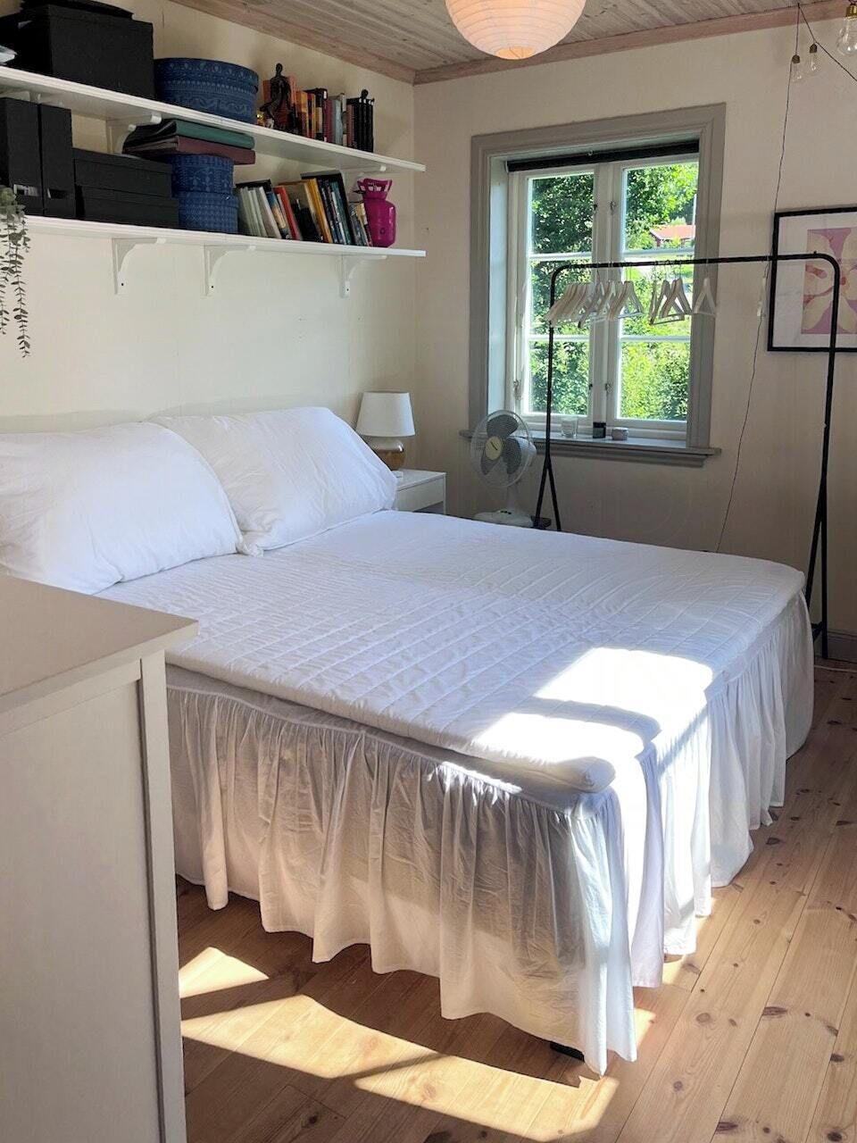 A bedroom with a bed, a bedside table, a lamp, a window, and a fan.