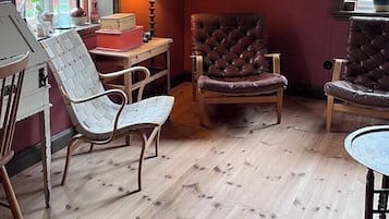 Una habitación con piso de madera, dos sillones de cuero, una silla blanca tejida, una mesita y una lámpara.