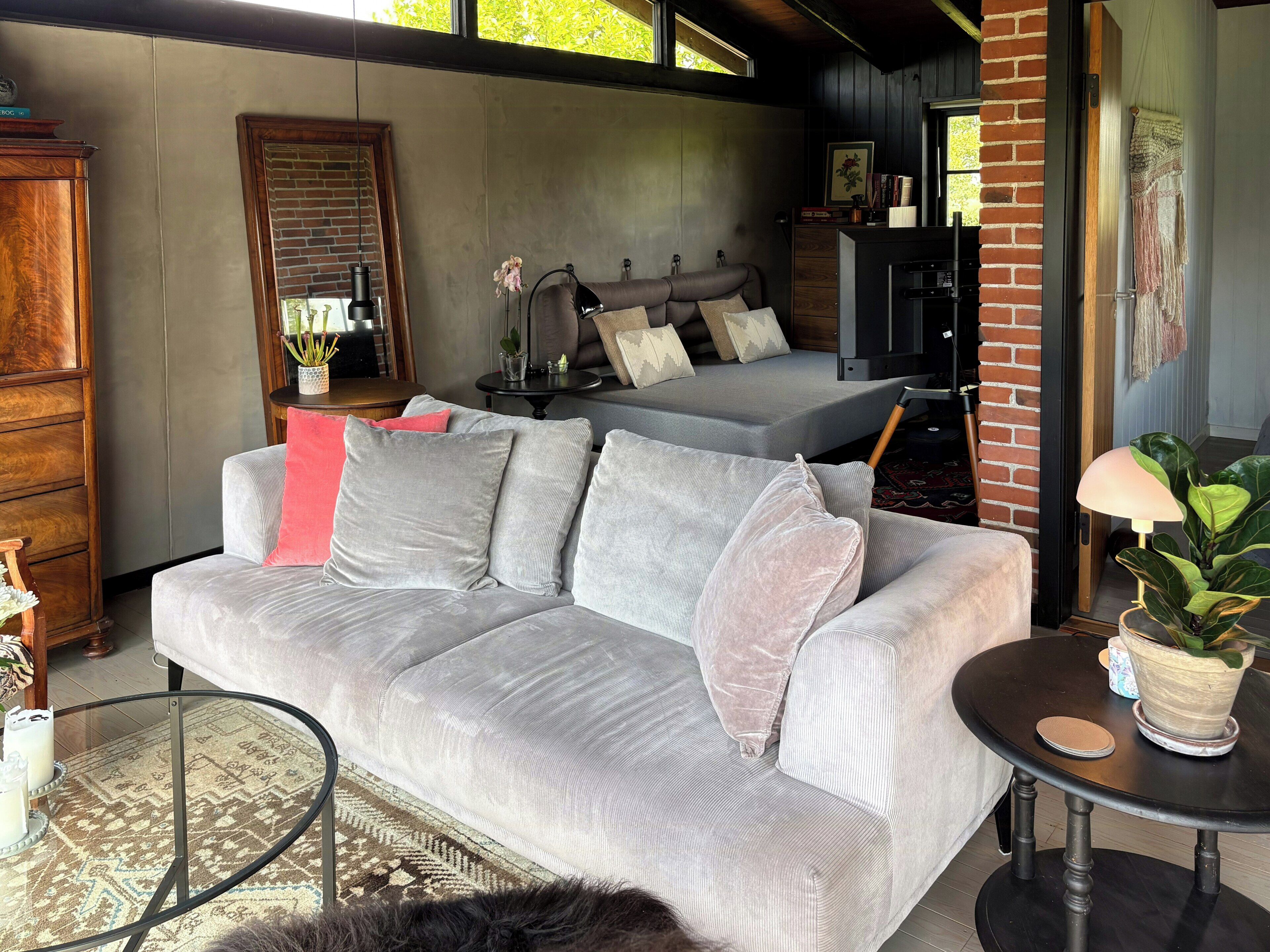 A modern living room with a grey sofa, a round glass coffee table, and a brick wall.