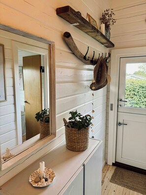 Ein Zimmer mit einem spiegelnden Holzboden, einem gewebten Korb mit Pflanzen, einer weißen Tür und einem rustikalen Regal mit Kerze und getrockneten Blumen.