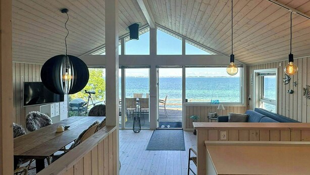 A modern interior with a wooden ceiling, large windows, a dining area, and a view of the sea.