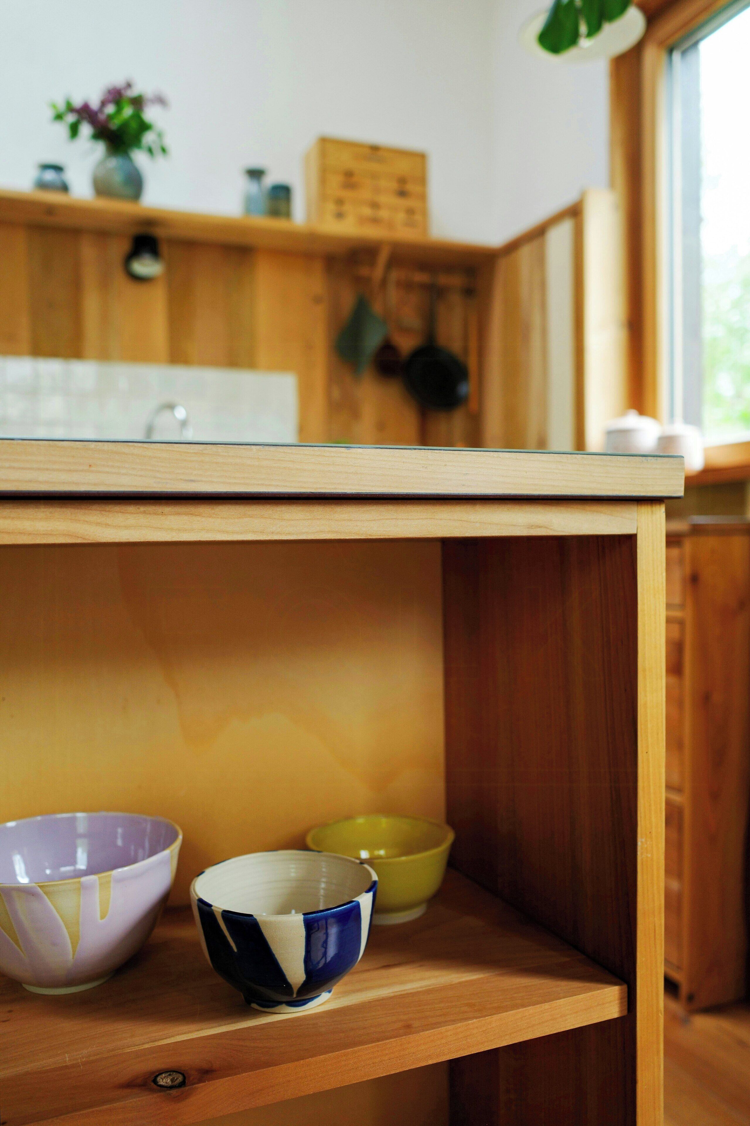 A wooden shelf with three bowls of different colors.