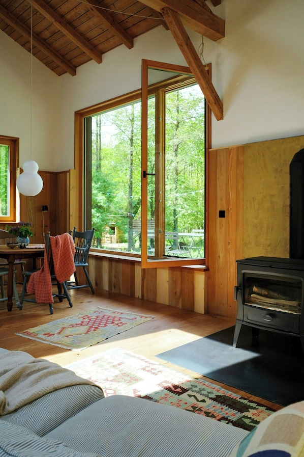 A cozy cabin interior with a large window, wooden walls, a fireplace, and a dining area.