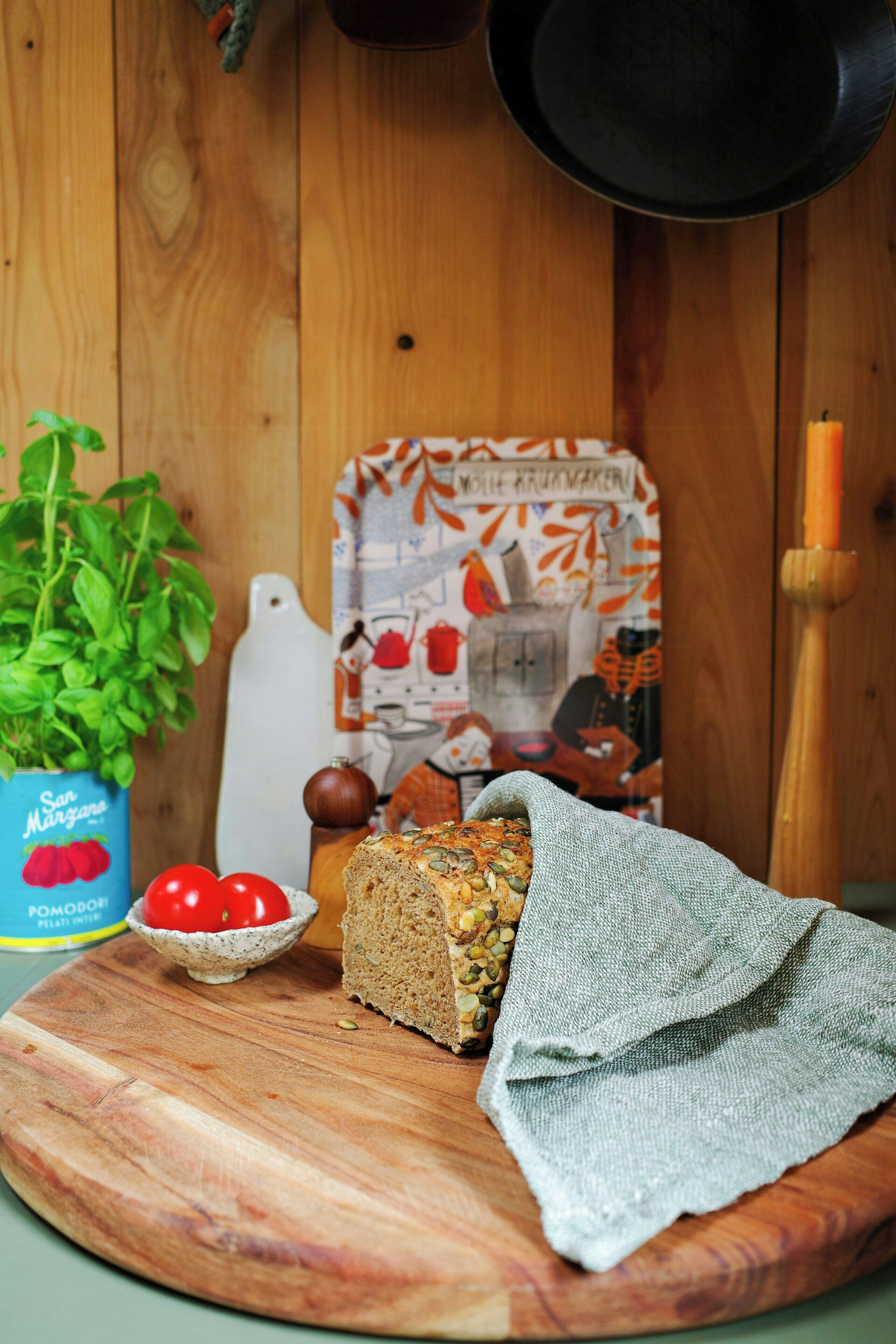 Ein Schneidebrett mit einem Brotlaib, einer Tomatenschale und einer Topfpflanze.