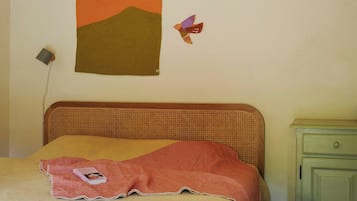 A bed with a headboard, a wall hanging, a lamp, a basket, and a nightstand.