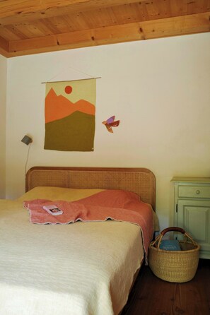 A bed with a headboard, a wall hanging, a lamp, a basket, and a nightstand. - Creatively converted wooden shed in the forest (Palling)
