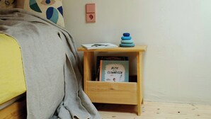 A bedroom with a wooden ceiling, a bed with a grey blanket, a bedside table with a book, and a wall-mounted light. - Creatively converted wooden shed in the forest (Palling)