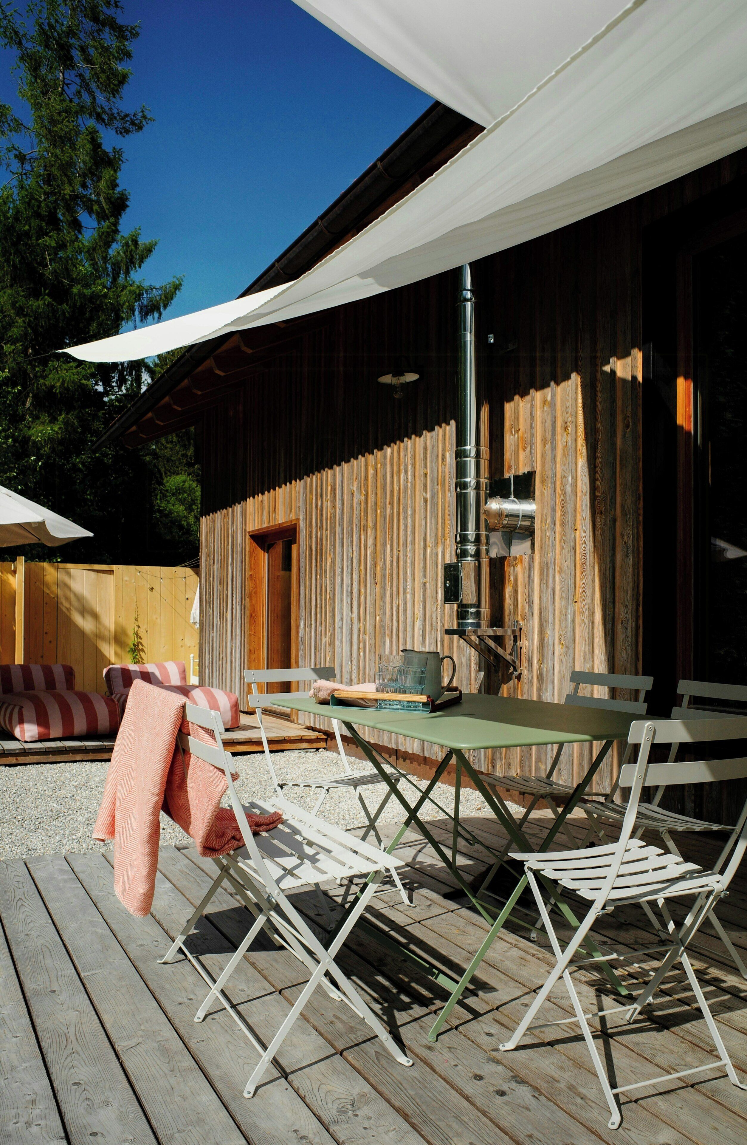 An outdoor patio with a table and chairs, a wooden fence, and a building in the background.