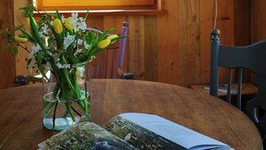 A wooden table with a book and a vase of flowers. - Creatively converted wooden shed in the forest (Palling)