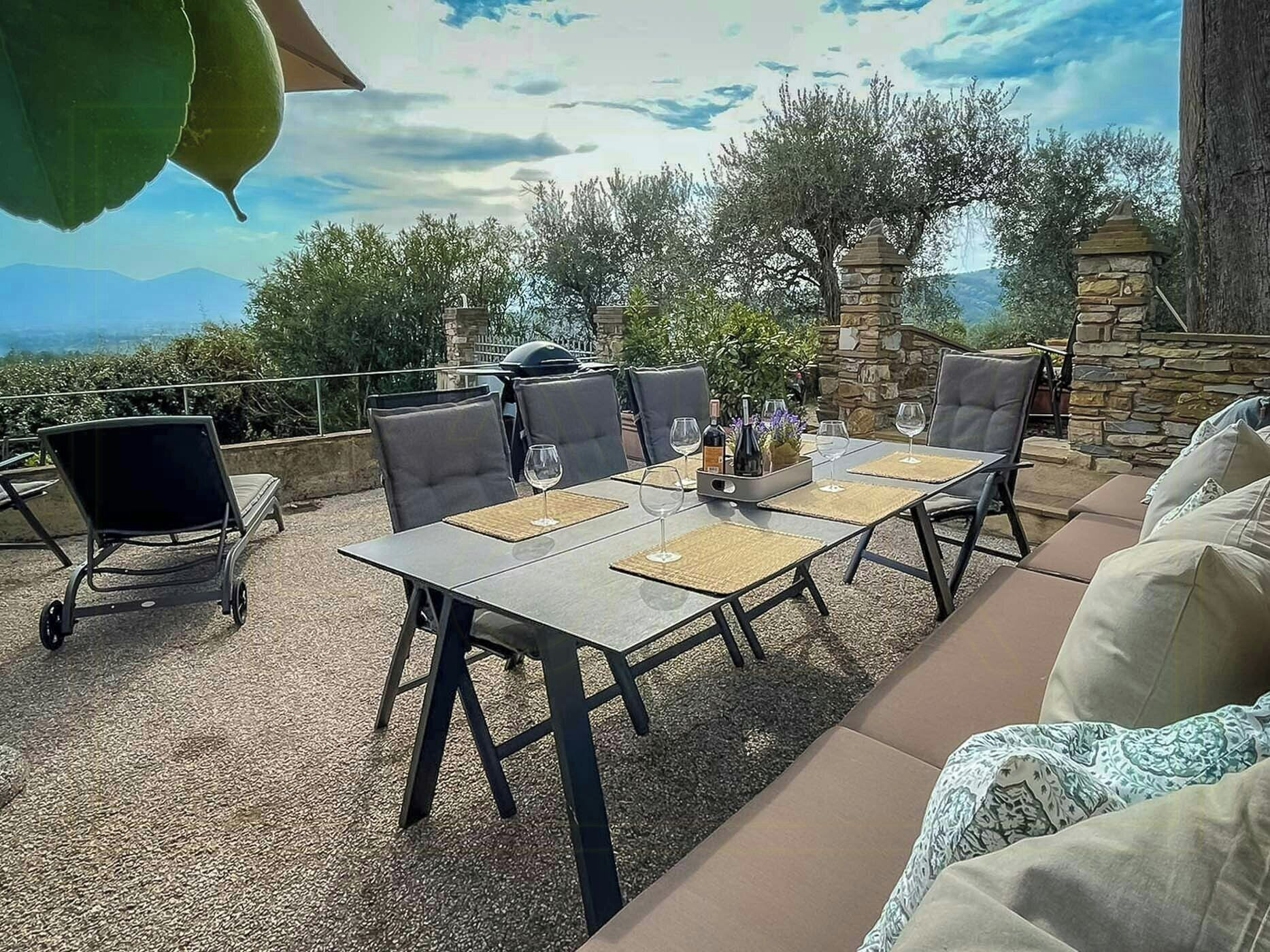 An outdoor patio with a table set for dining, surrounded by stone walls and greenery.
