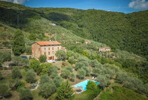 Eine Villa an einem Hang mit Swimmingpool, Steinbauten und umliegender Bepflanzung.