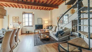 Een ruime woonkamer met een houten plafond, een bank, een bijzettafeltje en een trap.