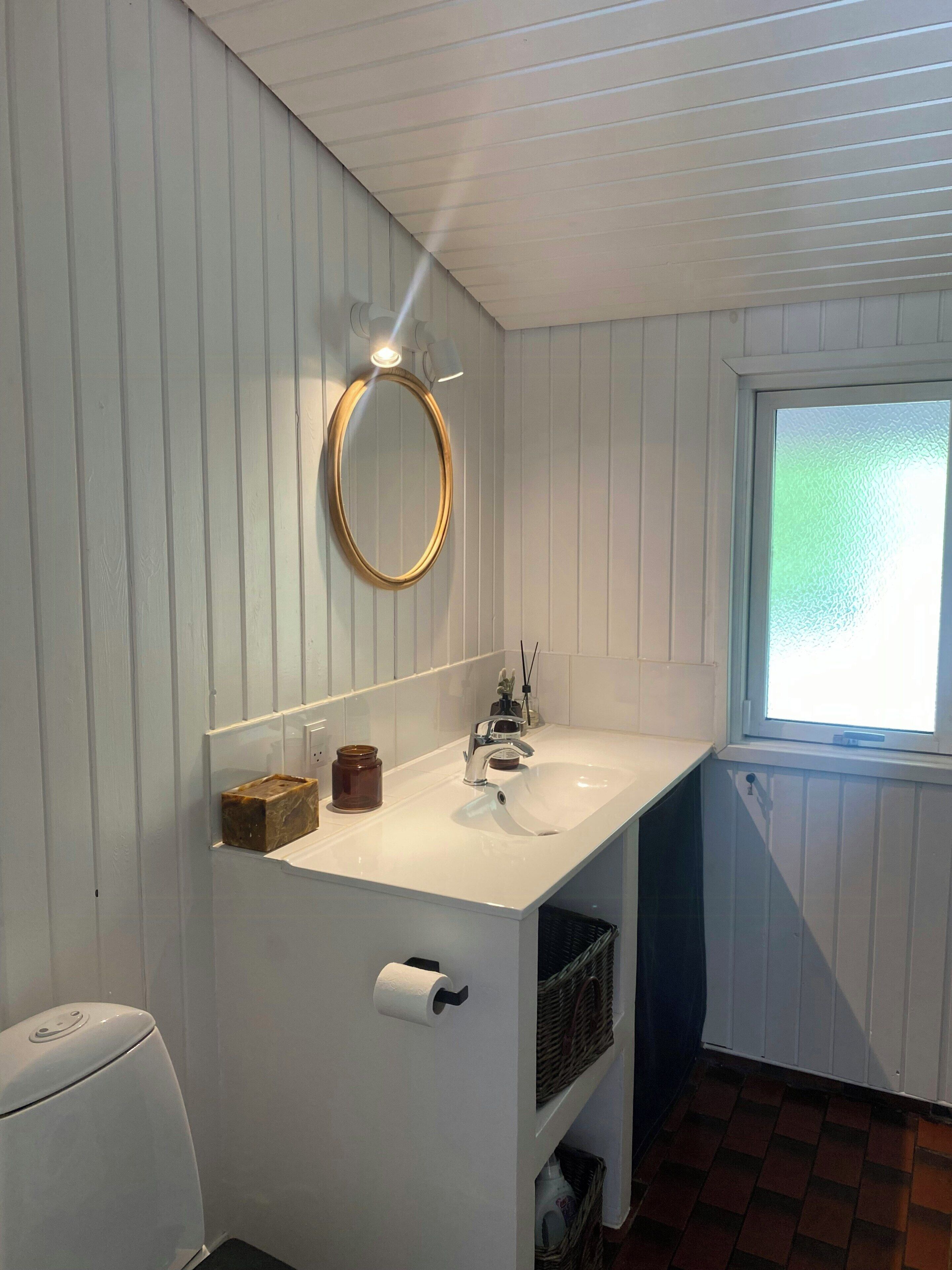 A bathroom with a white sink, a mirror, a toilet, and a window.