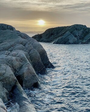 Litoral rochoso com o sol se pondo ao fundo.