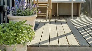 Eine Holzterrasse mit Pflanzkübeln, einer Holzbank und einer gepolsterten Sitzecke.