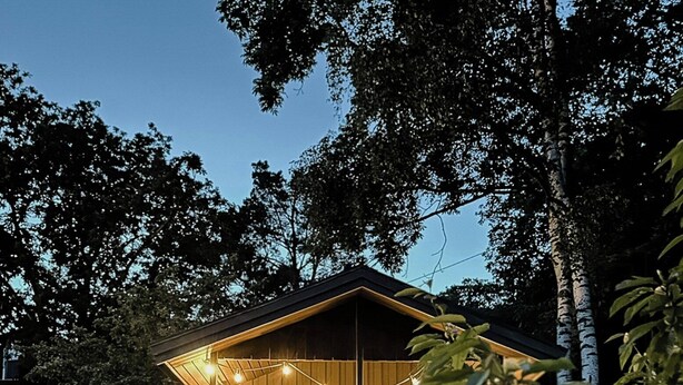 Eine Holzhütte mit Veranda, Lichterketten und einem Kiesweg, der dorthin führt.