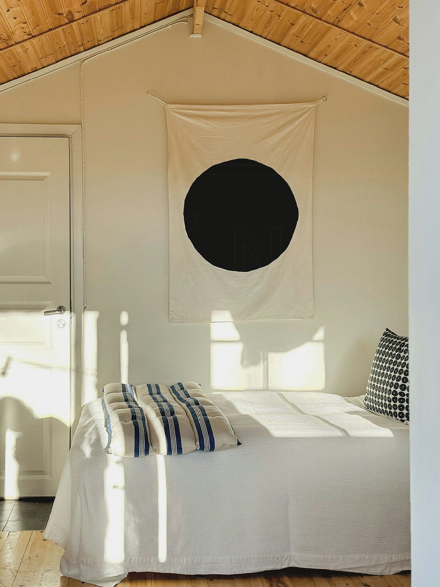 A bedroom with a bed, a door, a window, and a circular wall decoration.