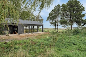 A modern house with a covered patio, surrounded by greenery and trees.