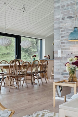 A dining area with wooden chairs, a table, hanging pendant lights, and a brick wall.