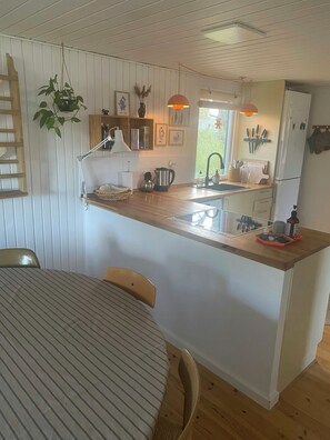 Una cocina compacta con una isla central, suelo de madera y un área de comedor con manteles a rayas.