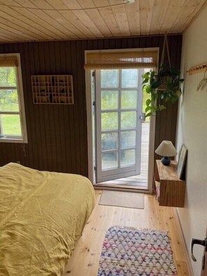 Un dormitorio con cama, ventana, puerta que da al exterior y una mesita con lámpara.