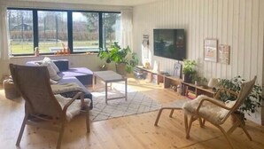 Uma sala de estar com sofá, duas poltronas, uma mesa de centro, televisão e estante de livros.