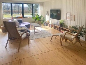 Ein Wohnzimmer mit einer Couch, zwei Sesseln, einem Couchtisch, einem Fernseher und einem Bücherregal.