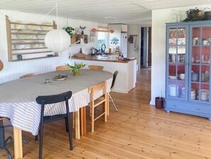Ein Essbereich mit einem runden Tisch, Stühlen, einem Schrank mit Glastüren und einer Küche im Hintergrund.