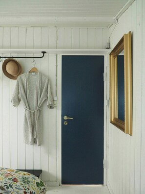 Ein Zimmer mit einer dunkelblauen Tür, einem hängenden Robe, einem Hut und einem Spiegel mit goldener Rahmung.