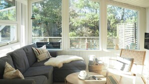 A cozy living room with a gray sofa, a round coffee table, and a wooden chair. Large windows offer a view of trees and a balcony. - Traditional holiday home at Cold Hawaii (Thisted)