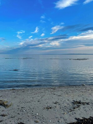 Ein Strand mit klarem Wasser, weiter Ferne und vereinzelten Trümmern.