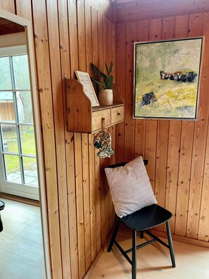 Ein Zimmer mit Holzwandverkleidung, einem schwarzen Stuhl, einem kleinen Regal mit Pflanze und Bilderrahmen sowie einem Gemälde an der Wand.