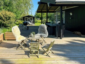 Eine Holzterrasse mit Gartenmöbeln, einem Grill und einer überdachten Lounge-Ecke.