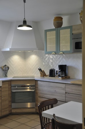 A kitchen with a herringbone tile backsplash, wooden cabinets, a built-in oven, a coffee maker, and a hanging pendant light. - Villa with heated pool near the Alpilles (Saint Rémy de Provence)