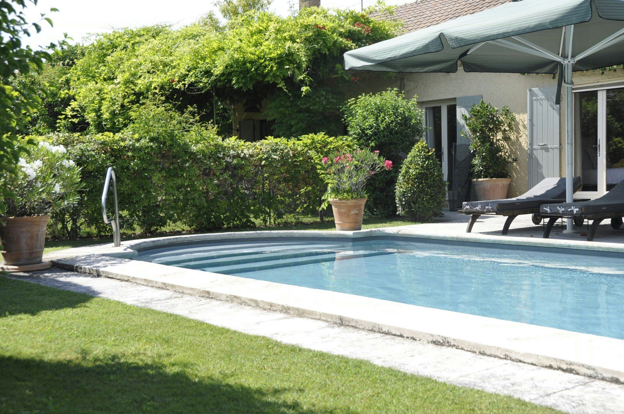 A swimming pool with a patio area, a covered seating area, and lush greenery.