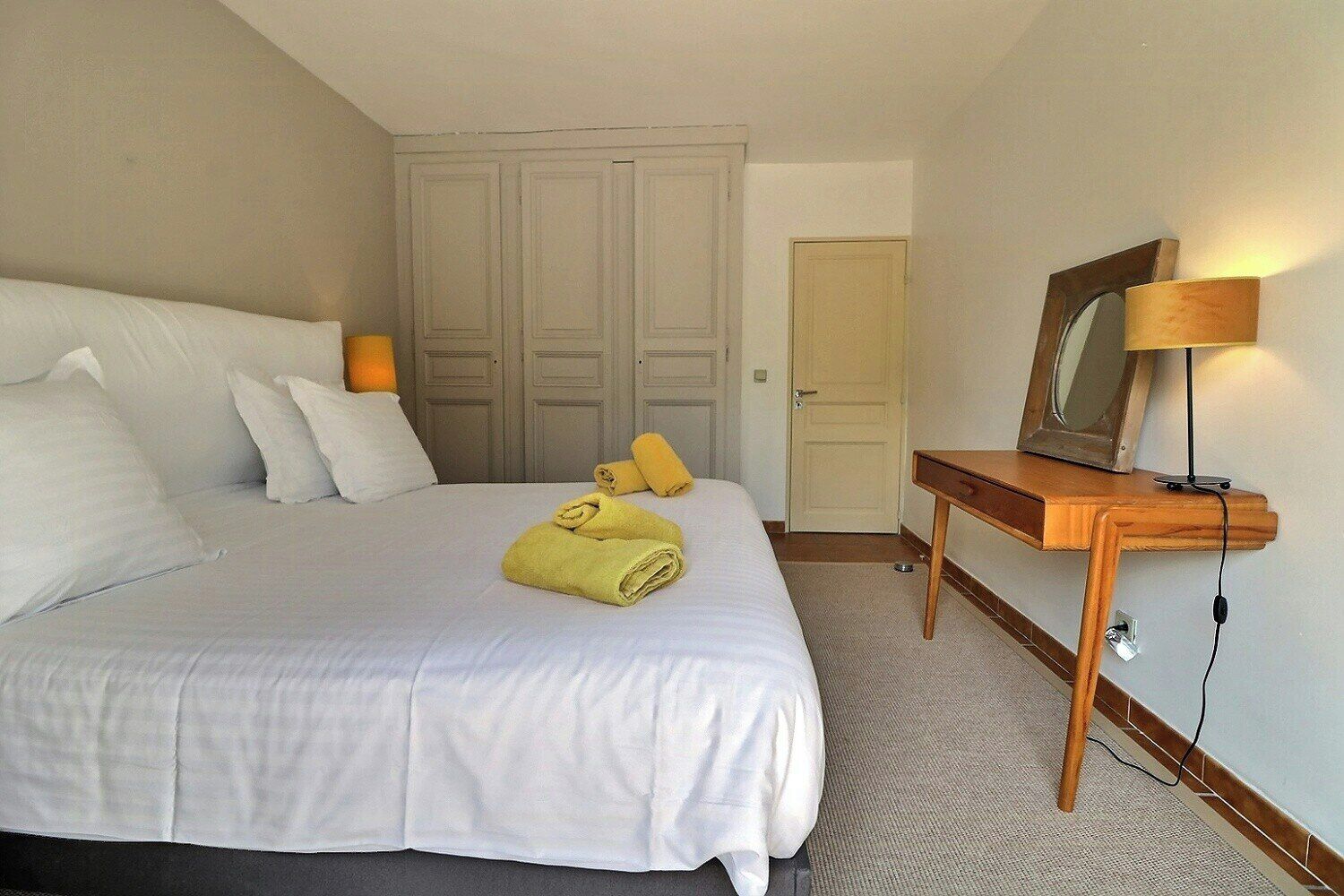A hotel room with a bed, a wooden nightstand, a lamp, and a door.
