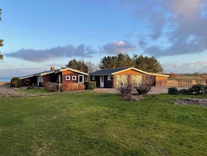 A row of cabins with a grassy field in front, a clear sky, and trees in the background. - Holiday home with pool and fjord views on Lundø (Højslev)