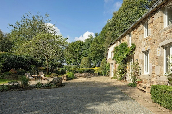 A stone building with a gravel driveway, a bench, and a small table with chairs.