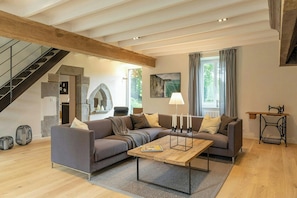 Un salon moderne avec un canapé d’angle, une table basse, un escalier et un mur en pierre.