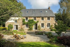 Une maison en pierre avec une allée pavée, un espace extérieur aménagé pour s’asseoir et un jardin.