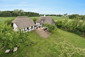 Ein Haus mit einem Reetdach, einem Garten und Blick auf die umliegende Landschaft.